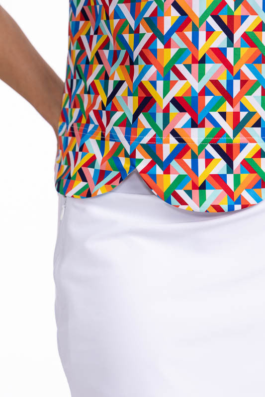 Front right side view of the On The Edge Sleeveless Golf Top in K All Day Print. The K All Day print is an abstract confetti-style mirrored K-shaped pattern in red, orange, yellow, green, blue, black and white. This top features a low mock neck, back zipp