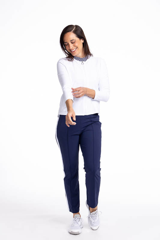 Full front view of a smiling woman wearing the Zip It Up Party Cardi in White and the Tailored Track Golf Pants in Navy Blue. This is a solid white cardi with a zip front, two pockets (one with built-in tee holders), and a rounded neckline.
