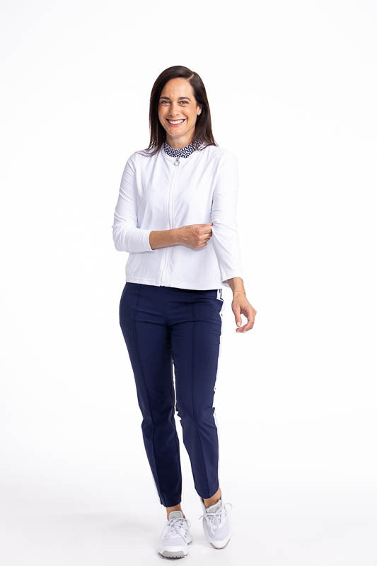 Full front view of a smiling woman wearing the Zip It Up Party Cardi in White and the Tailored Track Golf Pants in Navy Blue. This is a solid white cardi with a zip front, two pockets (one with built-in tee holders), and a rounded neckline.