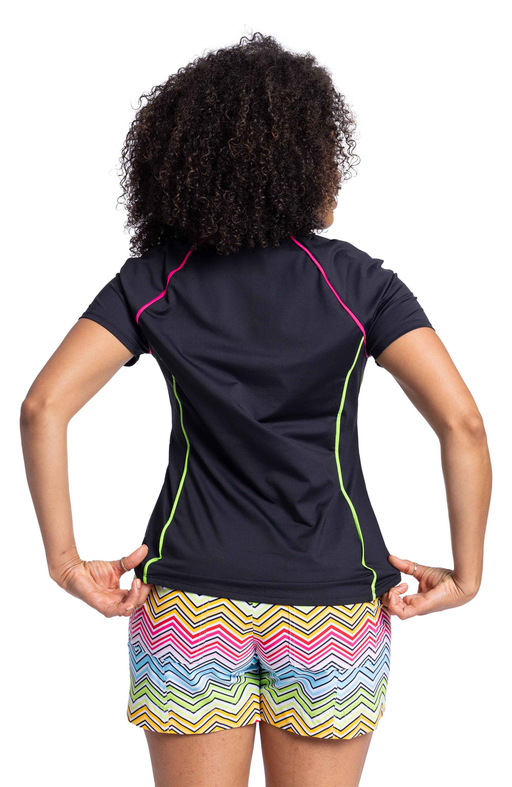 Back side of woman wearing black golf shirt with pink and yellow piping and multicolored golf shorts