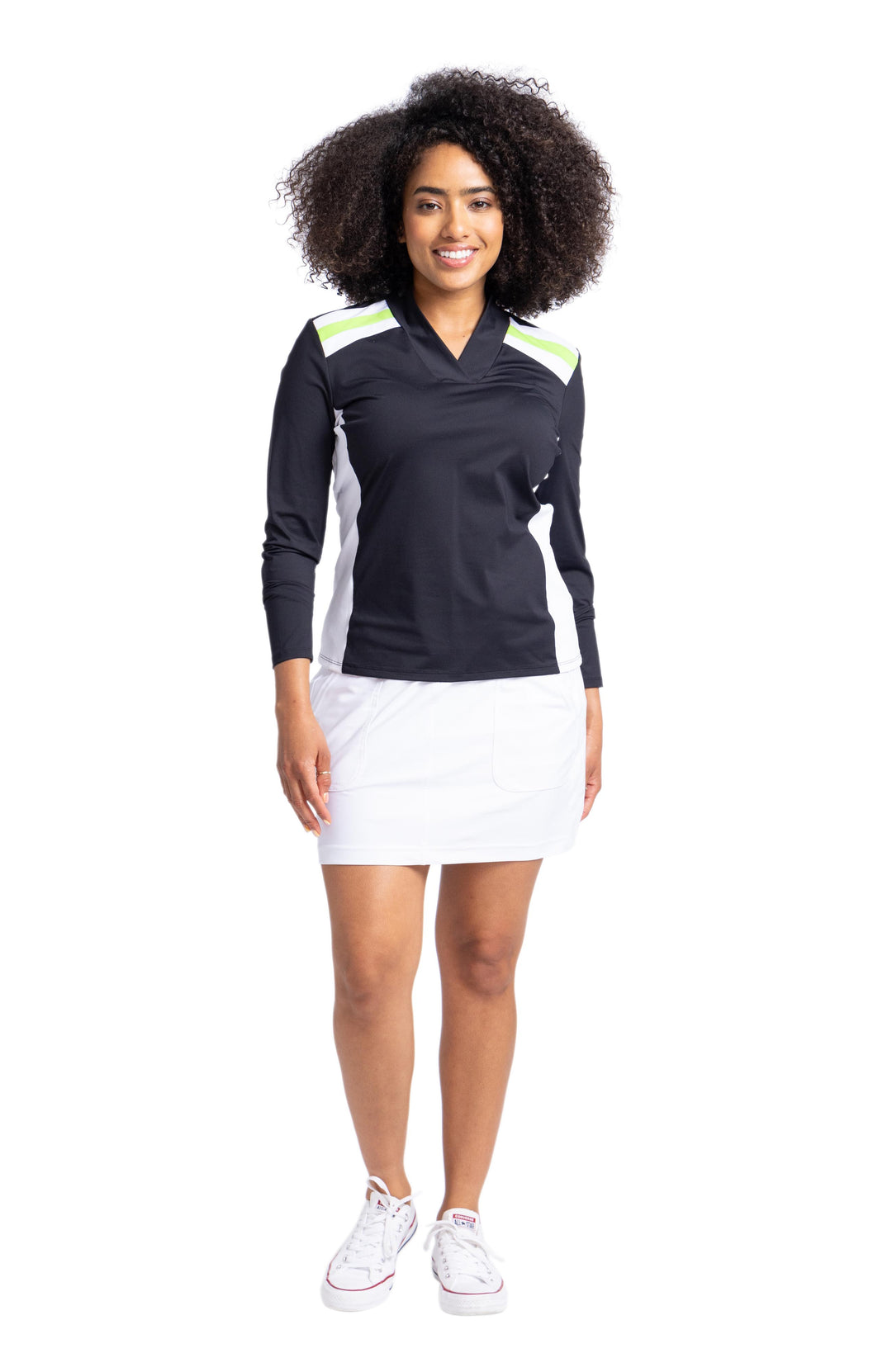 Full view of a woman smiling wearing a black longsleeve top with white and green stripes on shoulders and white contrasting side panels. She's also wearing a white skort. 