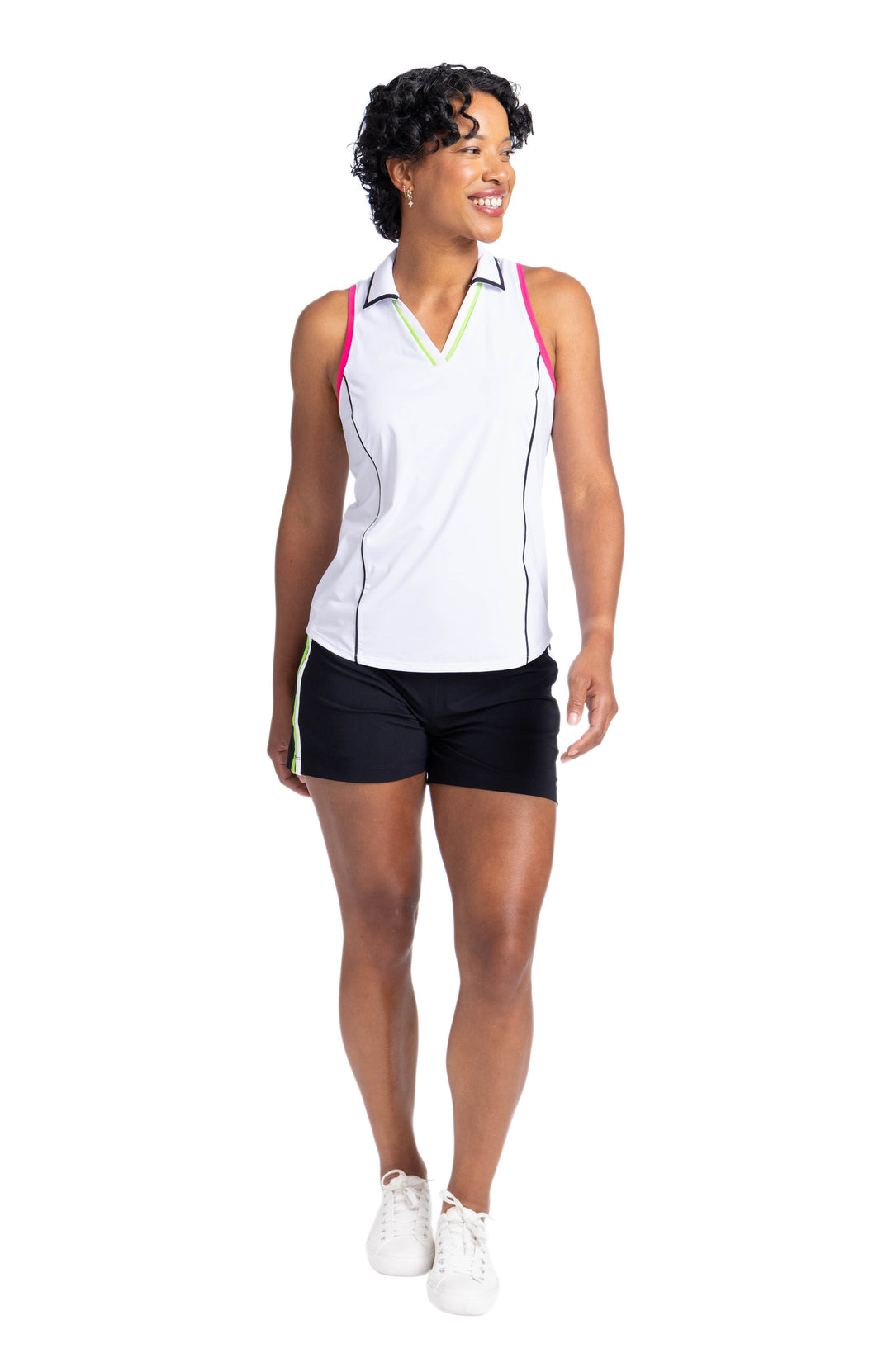 Full view of a woman wearing a white sleeveless top with black trim princess seams and around the collar. Pink binding around the armholes and green trim around the V-neck. She is also wearing black shorts.