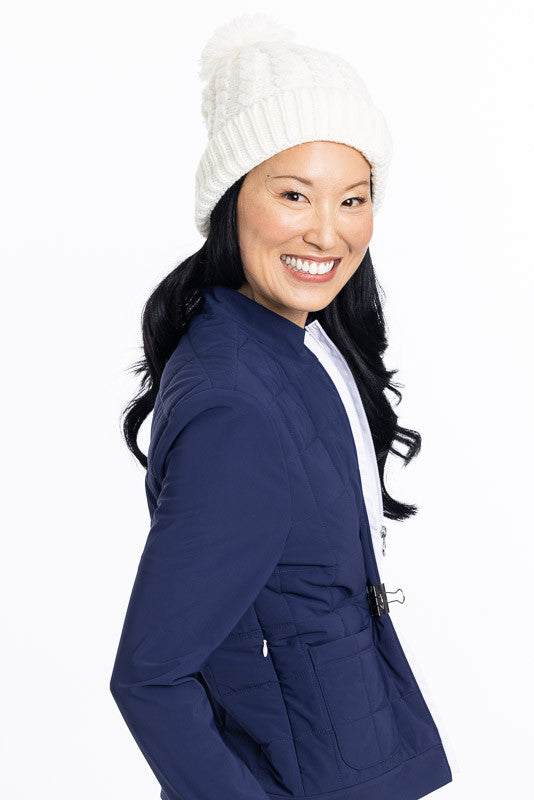 Smiling woman looking over her right shoulder wearing a navy blue Quilted and Cozy Jacket and a white knit cap
