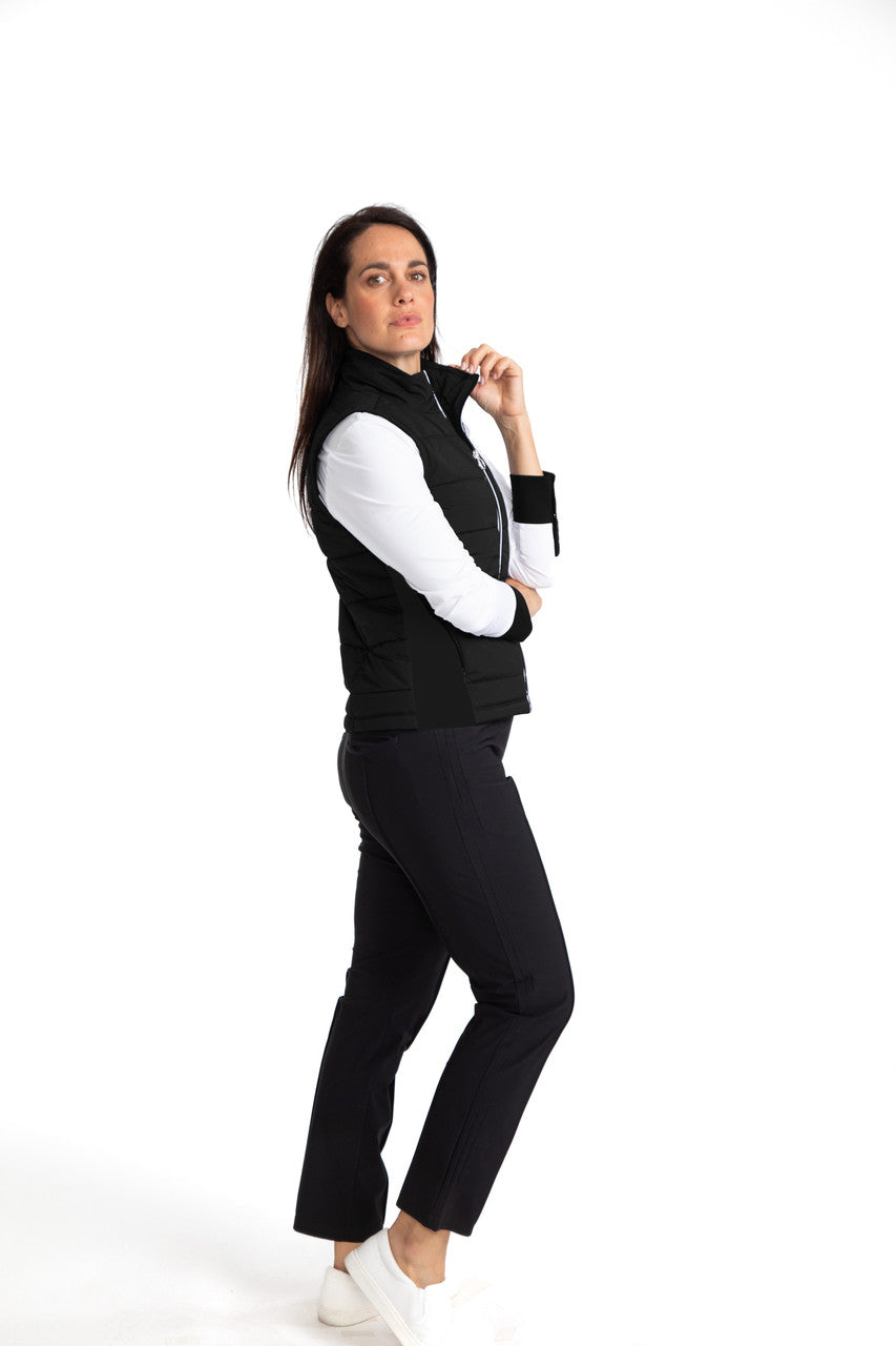 Right side view of a woman golfer wearing the Take The Chill Off Vest in Black, the Cool and Covered in White, and the Smooth Your Waist Crop Pants in Black. 