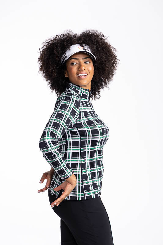 Right side view of a smiling woman wearing the Keep It Covered Long Sleeve Golf Top in Tartan Plaid and the No Hat Hair Visor in white.