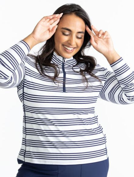 Smiling woman with hands on either side of her forehead wearing the Keep It Covered Long Sleeve Golf Top in Shutter Stripe. This pattern is a grouping of four horizontal, navy blue stripes with white space in between from top to bottom on this top.