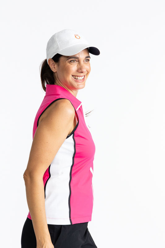 Right side view of a smiling woman wearing the We've Got You Covered Hat in White and the Swing Away Sleeveless Golf Top in Preppy Pink. This is a solid Preppy Pink top trimmed in black around each armhole, a white front zipper, and a white side section t