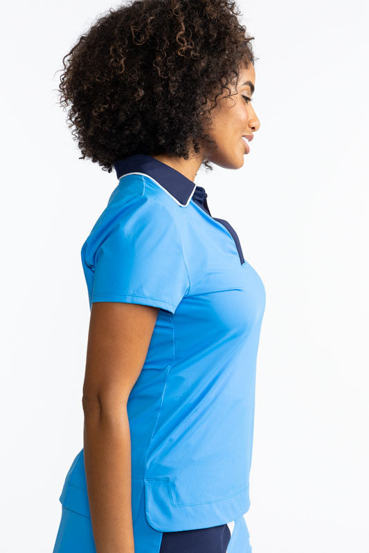 Right side view of a woman wearing the Classic and Fantastic Short Sleeve Golf Top in French Blue. This top is a solid French blue with a navy blue collar trimmed with white and a navy blue V-neck front.