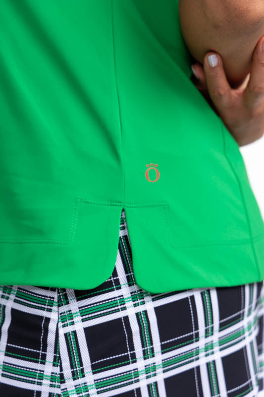 Close left side view of the hemline on the Classic and Fantastic Short Sleeve Golf Top in Rye Grass Green. This is a solid green top with a contrasting white V-neck and a white collar with black trim on the collar's edge.