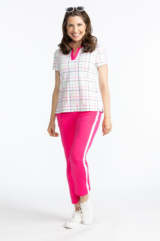 Full front view of a smiling woman with sunglasses on her head wearing the Smooth Your Waist Golf Crop Pants in Preppy Pink and the Classic and Fantastic Short Sleeve Golf Top in Tattersall Plaid. This top has a Preppy Pink V-neck, with the collar also tr
