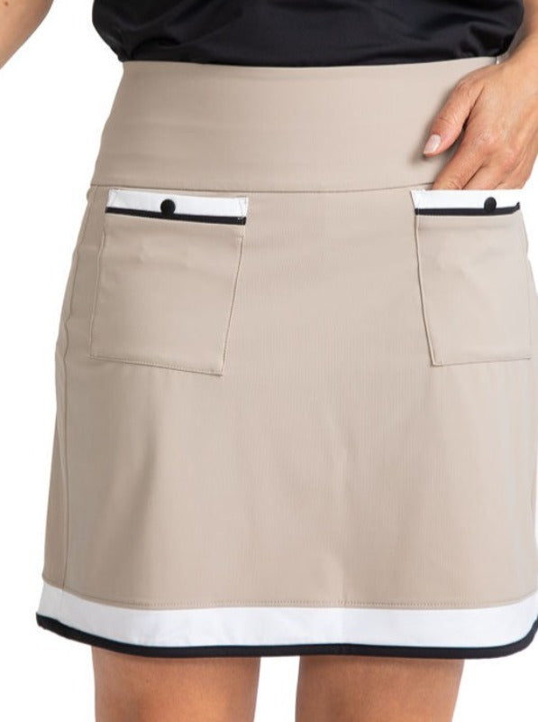 Tight front view of the Tee to Tea Golf Skort in Sand.  This skort has white and black accents across the top of each front pocket, a large, white band, and a smaller, black band around the hemline of this skort.