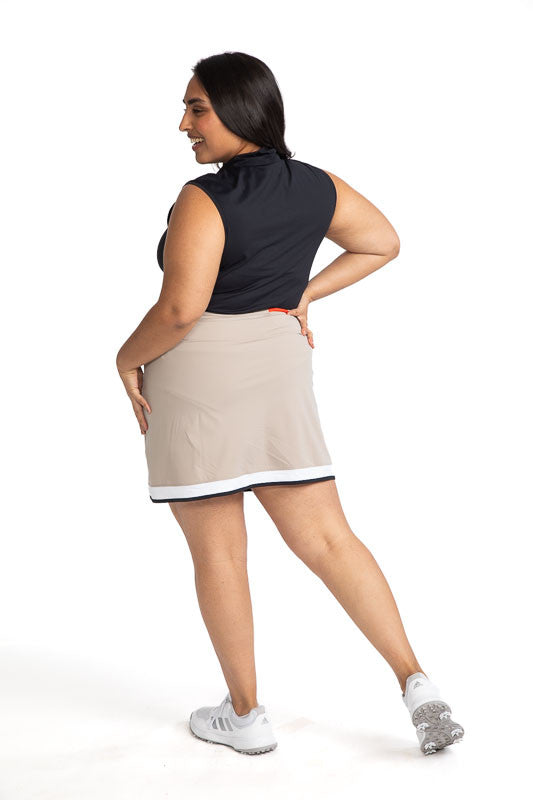 Full back view of a woman wearing the Tee to Tea Golf Skort in Sand.  This skort has white and black accents across the top of each front pocket, a large, white band, and a smaller, black band around the hemline of this skort.
