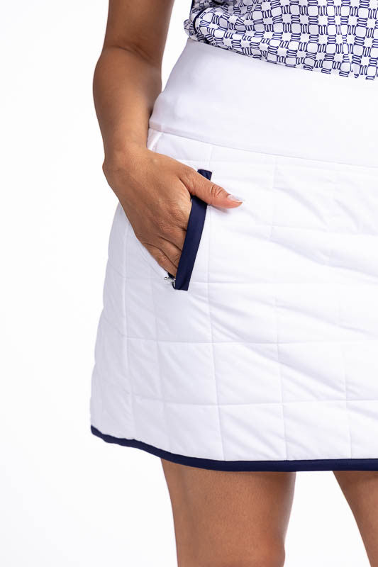 Front and right side view of one of the front zippered pockets on the Quilted and Cozy Golf Skort in White/Navy Blue. This is a white, quilted skort with navy blue trim around the hemline and two front zippered pockets with navy blue trim. There is also a
