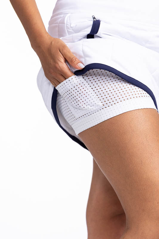 Right side view showing one of the ball pockets on the white, breathable mesh shorties on the Quilted and Cozy Golf Skort in White/Navy Blue. This is a white, quilted skort with navy blue trim around the hemline and two front zippered pockets with navy bl
