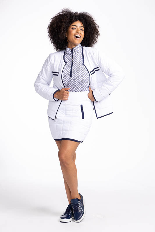 Full front view of a smiling woman wearing the Quilted and Cozy Golf Skort in White/Navy Blue, the Keep It Covered Sleeveless Golf Top in Tees Please, and the Polished for Play Jacket in White/Navy Blue. This is a white, quilted skort with navy blue trim 