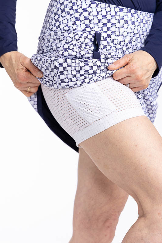 Close right side view showing the built-in, white, breathable mesh shorties with built-in ball pocket on the Quilted and Cozy Golf Skort in Tees Please print. This is a navy blue and white printed skort with a navy blue band around the hemline and accents