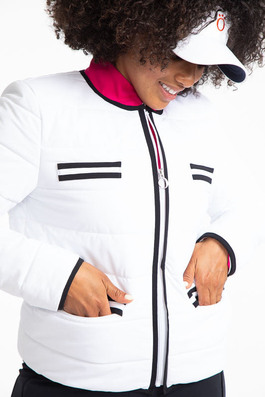 Tight front view of a woman golfer wearing the Polished for Play Golf Jacket in White. This jacket has black accents around the neckline and on each size of the front zipper, two decorative stripes, creating  faux breast pockets on each side, two stripes 