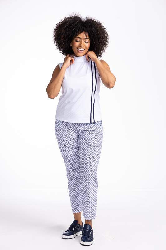 Full front view of a smiling woman wearing the No Break Sleeveless Golf Top in White and the Tailored Crop Golf Pants in Tees Please print. This is a white top with two vertical navy blue stripes from the left shoulder to the hem. This top also features a
