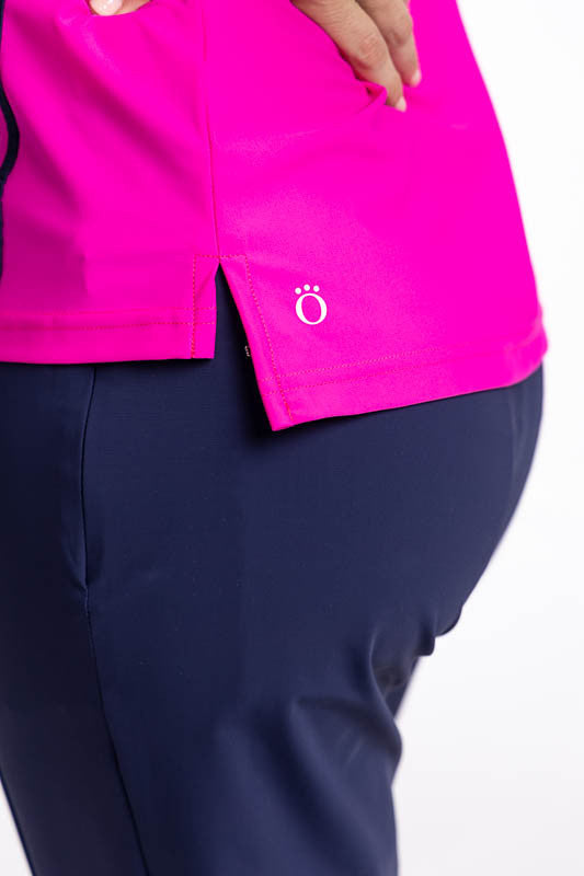 Close left side view of the hemline on the No Break Sleeveless Golf Top in Open Air Pink. This is a bright pink top with two vertical stripes in white and navy blue that run from the left shoulder to the hem. This top also features a mock collar and a bac