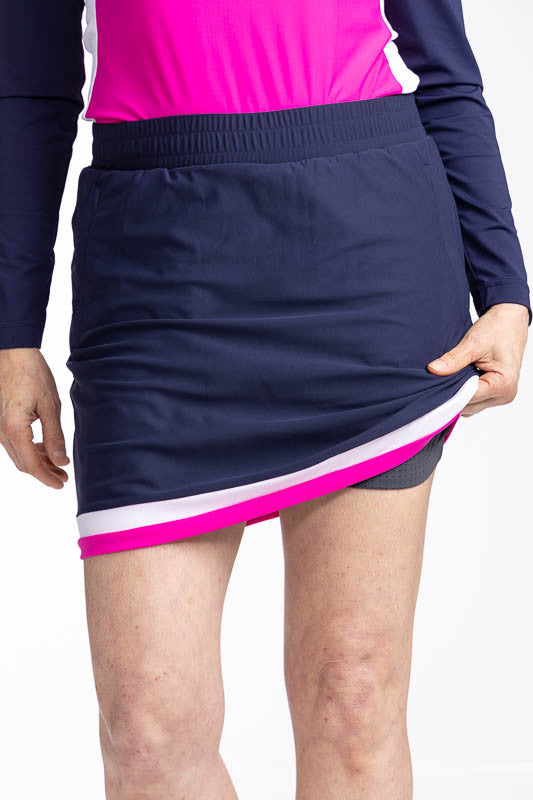 Close front view showing the dark grey built-in mesh, breathable shortie on the Comfy and Cozy Golf Skort in Navy Blue. This is a navy blue skort with two horizontal stripes around the hemline - one white and one open air pink. It also features two side z