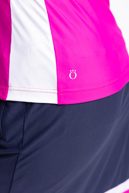 Close left side view of the hemline on the Cap to Tap Long Sleeve Golf Top in Open Air Pink. This top is a solid pink top with navy blue sleeves and neckline and white stretch rib sides.