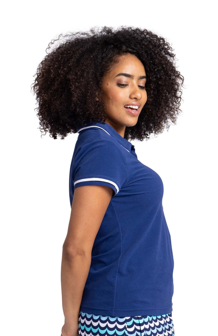 Side view of a woman wearing a short sleeve, navy blue top with white trim around the sleeves and collar.