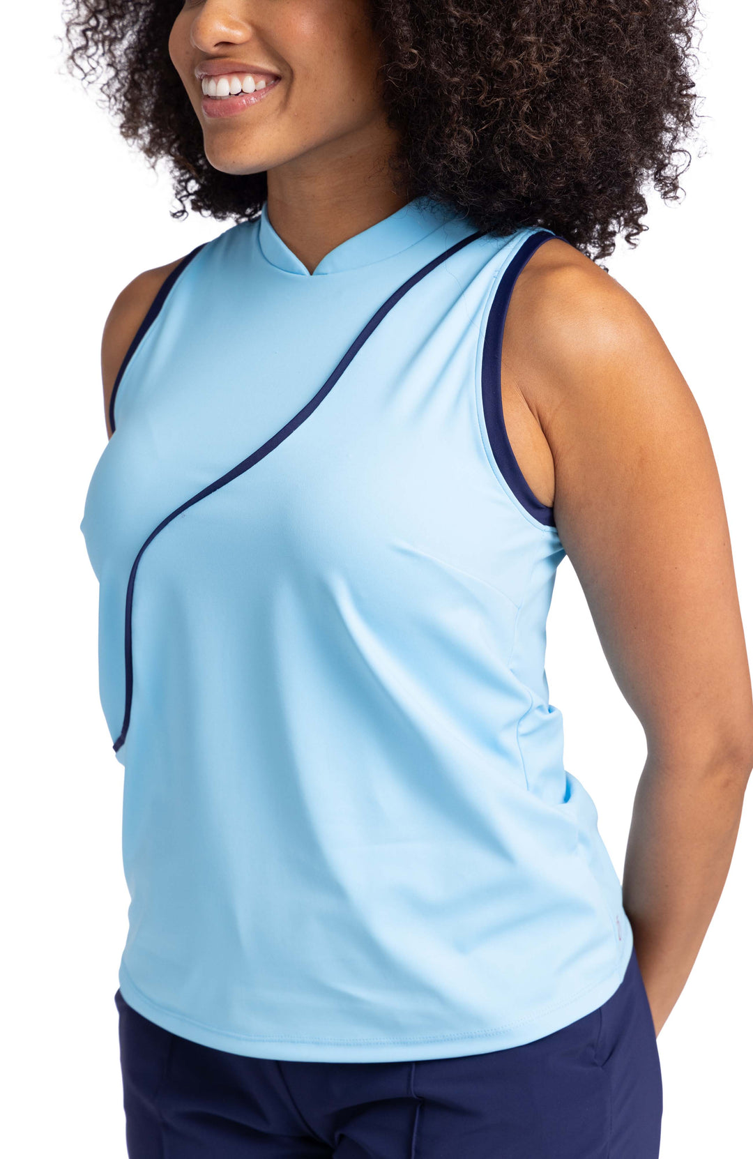 A woman wearing a light blue sleeveless top with navy blue contrasting trim on the armholes and a navy blue wavy seam down the front.