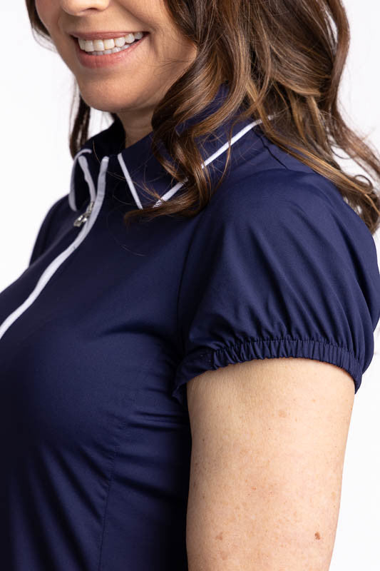 Close left side view of the slight gathering at the top of the sleeve on the Prettier Than A Polo Short Sleeve Golf Top in Navy Blue. This is a solid navy blue top with a quarter zip front with white piping around the collar. 