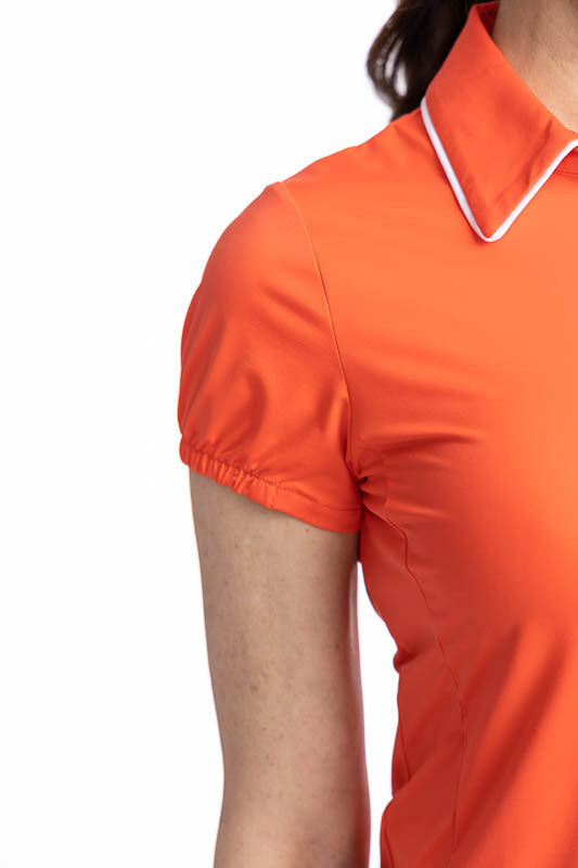 Close right side view of the gathering on the sleeve and the collar on the Prettier Than A Polo Short Sleeve Golf Top in Coral Red and the No Hat Hair Visor in White. This is a solid coral red top with a quarter zip front with white piping around the coll