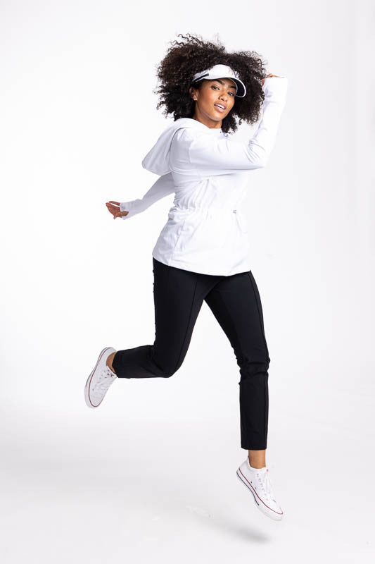 Full front and left side view of a woman wearing the Aprés 18 Anorak Long Sleeve Hoodie in white, the Aprés 18 Jogger Pants in black and the No Hat Hair Visor in white. 