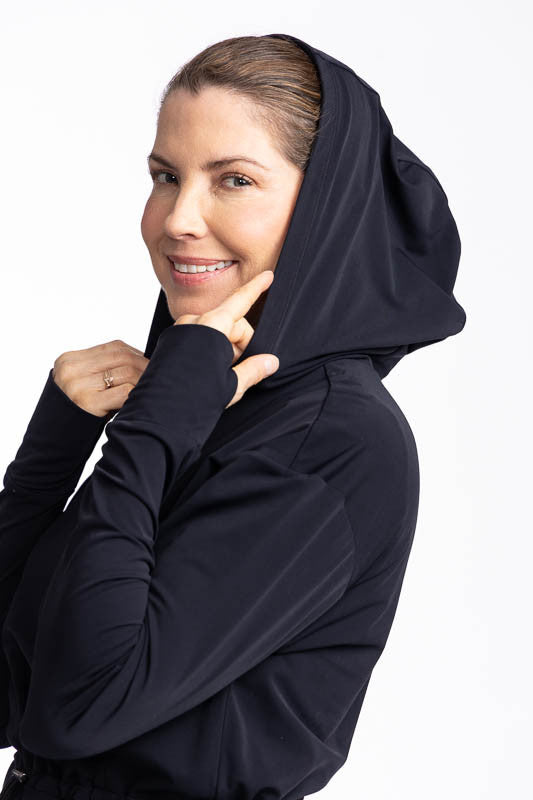 Close front and left side view of a woman wearing the Aprés 18 Anorak Long Sleeve Hoodie in black with the hood pulled up.