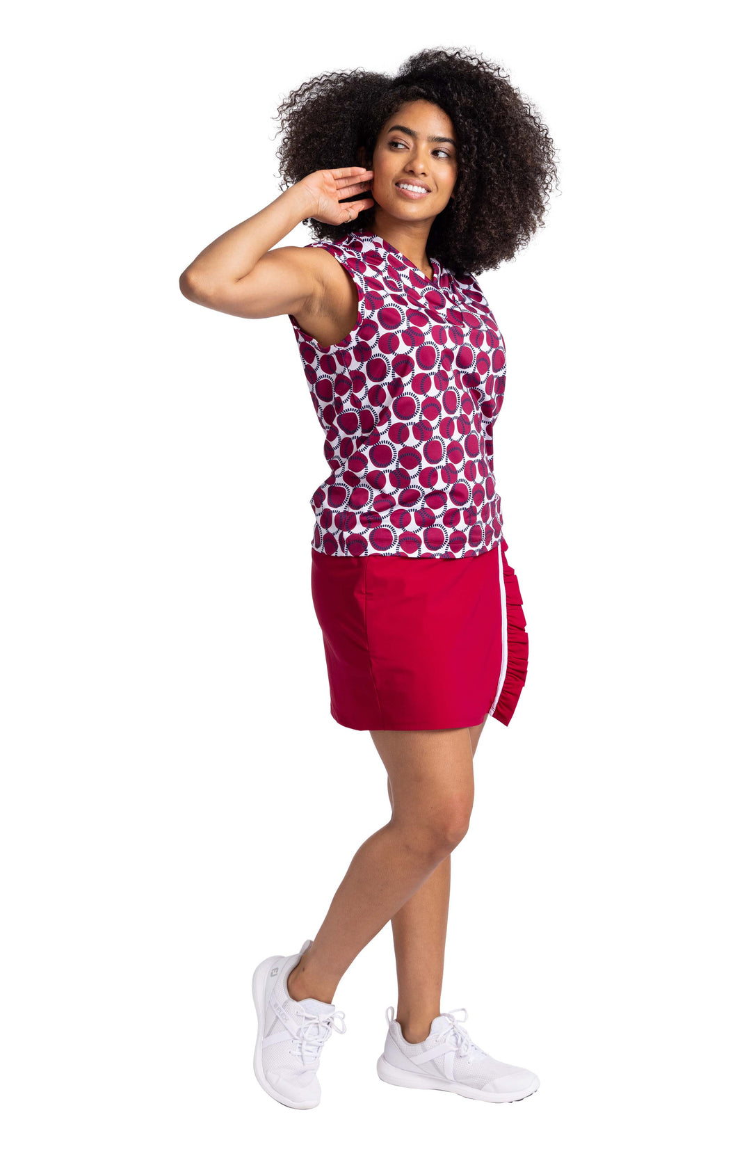 Three quarters view of a woman wearing a sleeveless, V-neck top with Bordeaux Red and navy blue circles on a white background pattern. The top is paired with the Ruffle In The Rough skort in Bordeaux Red. 