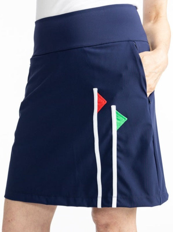 Close front view of the Flagstick Golf Skort in Navy Blue. This skort is a solid navy blue with two golf flagsticks on the front left side - one is a red flag and the other is a green flag. 