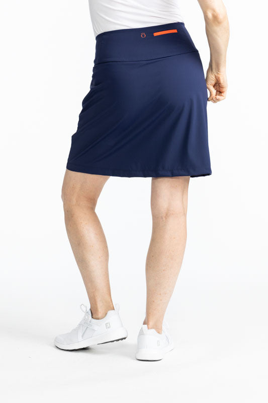 Full back view of the Flagstick Golf Skort in Navy Blue. This skort is a solid navy blue with two golf flagsticks on the front left side - one is a red flag and the other is a green flag. 