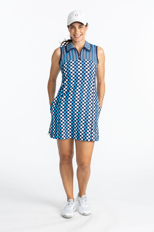 Full front view of a smiling woman golfer wearing the In The Cup Sleeveless Golf Dress in Check It Out and the We've Got You Covered Hat in white. The check it out print consists of French blue, black, and white in a checker board print. There are also na