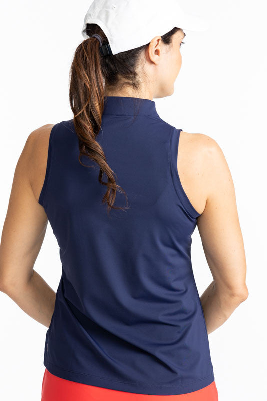 Back view of a woman wearing the We've Got You Covered Hat in White and the On Target Sleeveless Golf Top in Navy Blue. This top features a navy blue background with two thick stripes, one tomato red, and one white across the front just above the chest an
