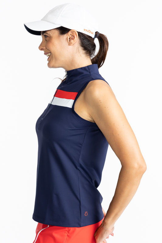 Left side view of a woman wearing the the We've Got You Covered Hat in White and the On Target Sleeveless Golf Top in Navy Blue. This top features a navy blue background with two thick stripes, one tomato red, and one white across the front just above the