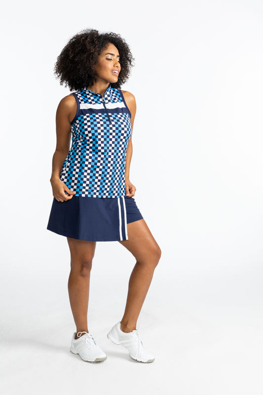 Smiling woman golfer wearing the Party Pleat Golf Skort in Navy  Blue and the On Target Sleeveless Golf Top in Check It Out print. This print is made up of French blue, navy blue, and white checks forming a vertical pattern and has one thick white stripe 