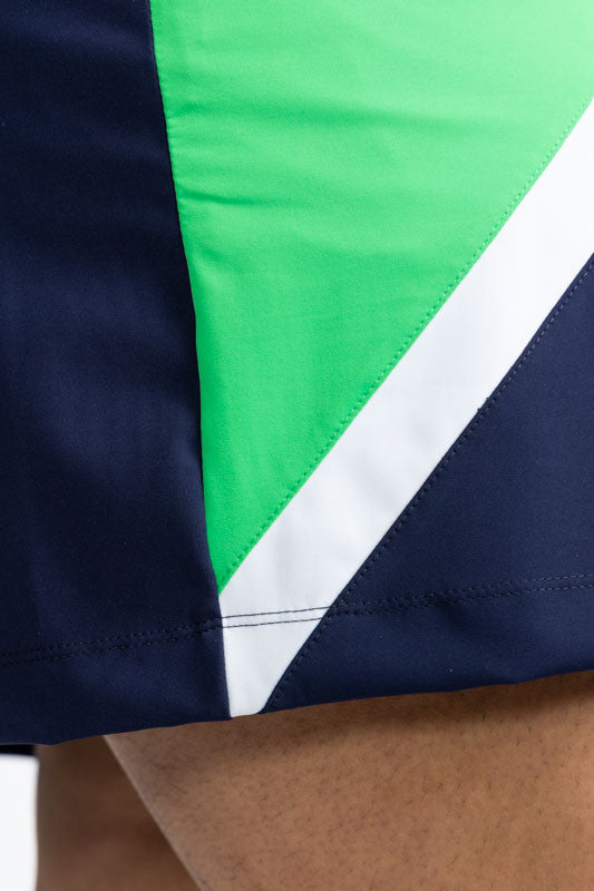 Close right side view of the hemline on the Tend the Flag Golf Skort in Navy Blue. In this view, you also get a close-up view of the diagonal white stripe and part of the Kelly green triangular section on a navy blue background.