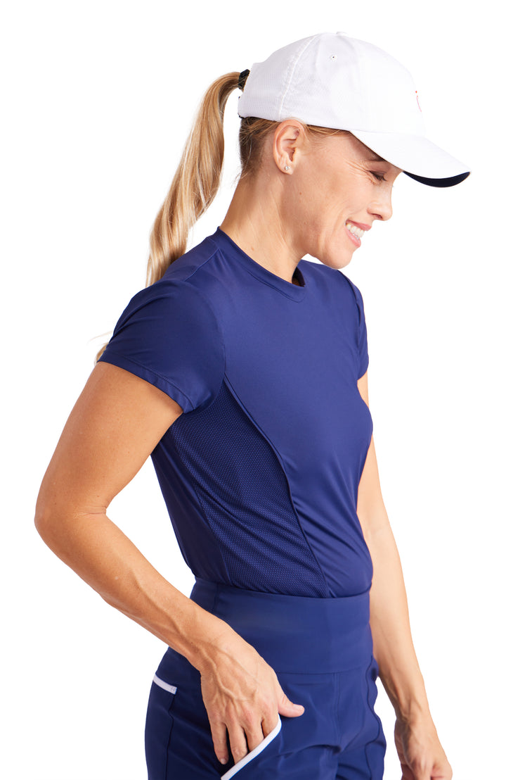 Side view of a woman wearing a short sleeve, navy blue top with front princess seams and side mesh panels.