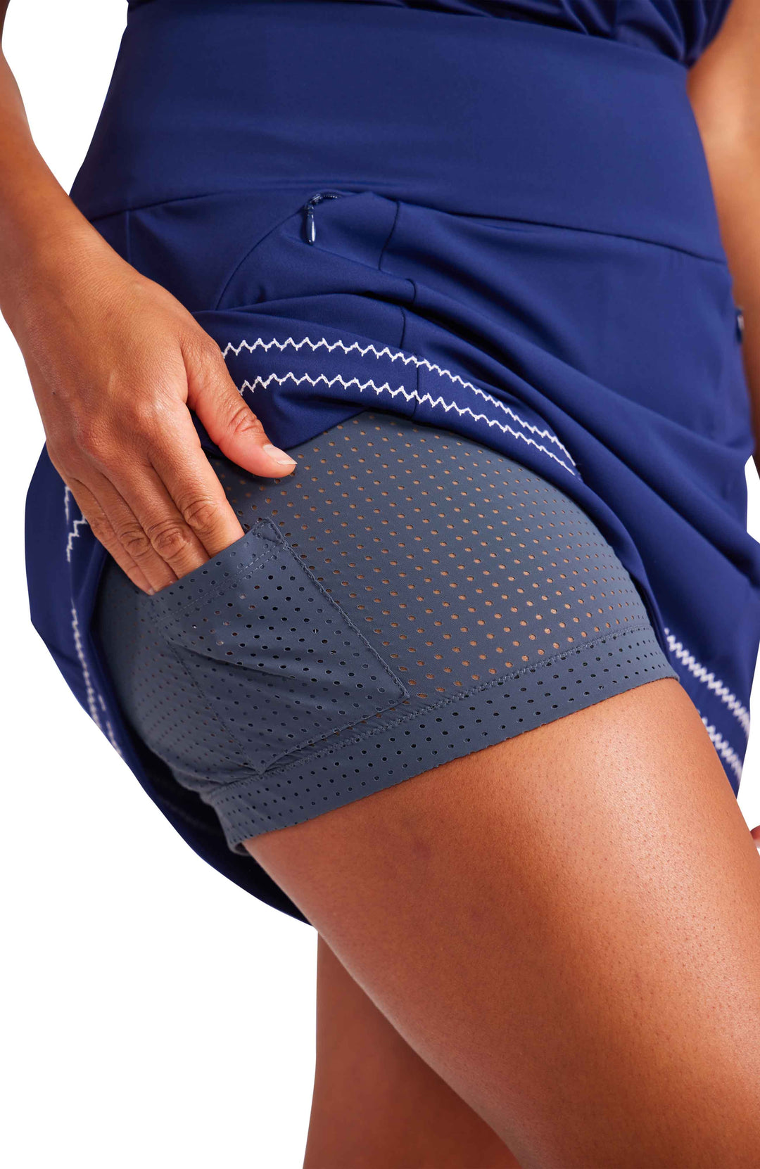 Close-up view of a woman putting her hand into the ball pocket of the grey mesh shorty that comes under the skort. 