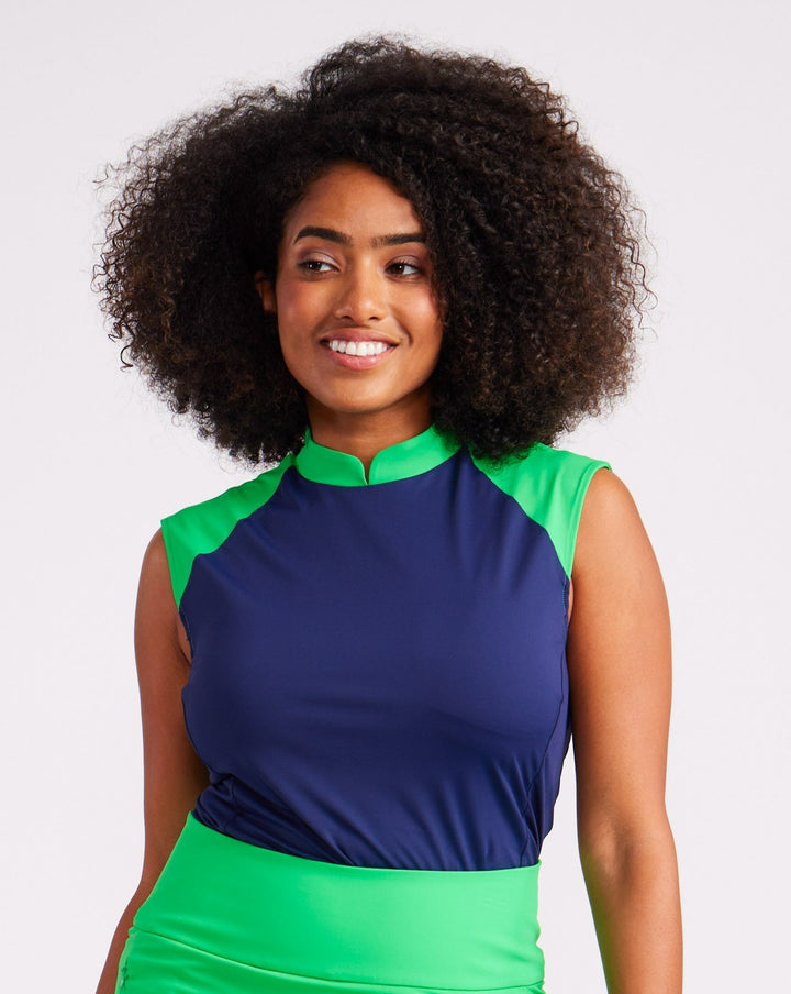Front facing view of woman is a navy sleeveless top with green shoulder and collar trim