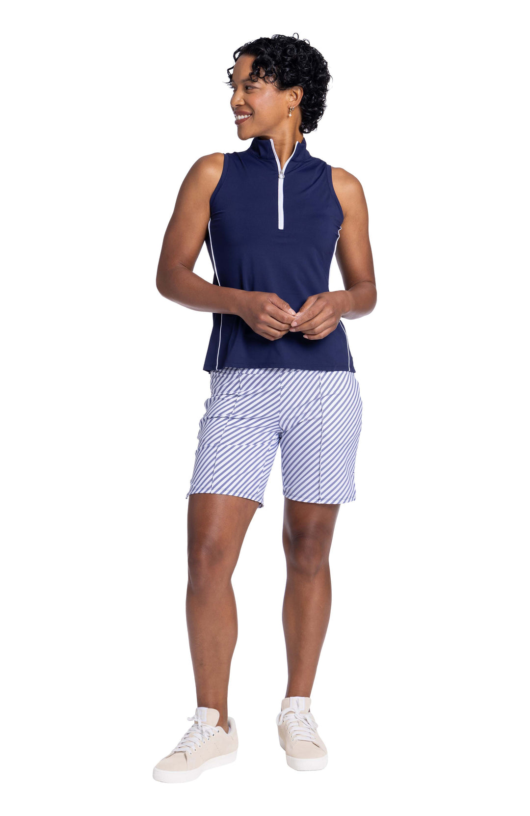 Full front view of a woman wearing the Keep It Covered Sleeveless Golf Top in navy blue and the golf glove friendly short in market stripe. 