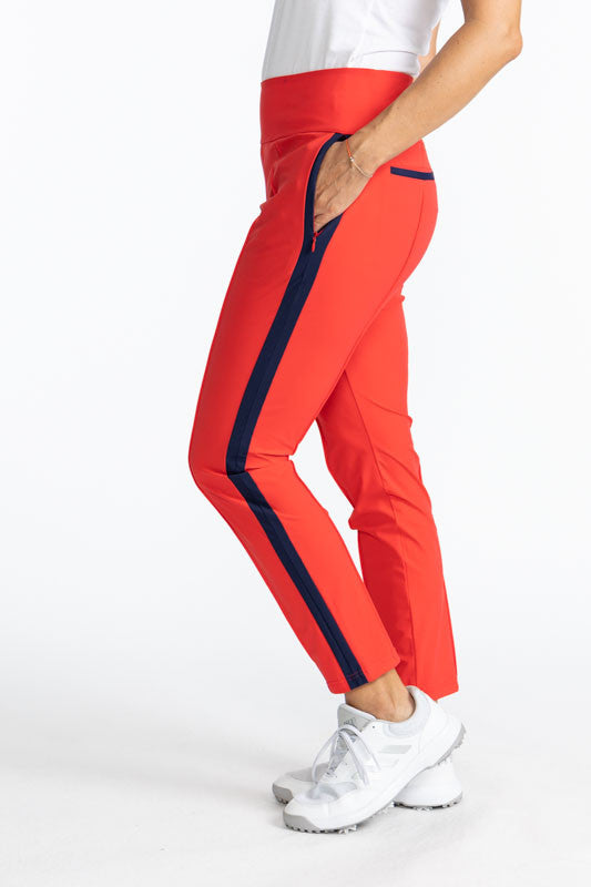 Full left view of the Tailored Track Golf Pants in Tomato Red. These pants are solid tomato red with a black stripe that runs down each side of the pants. There are also black accents on the two back pockets.
