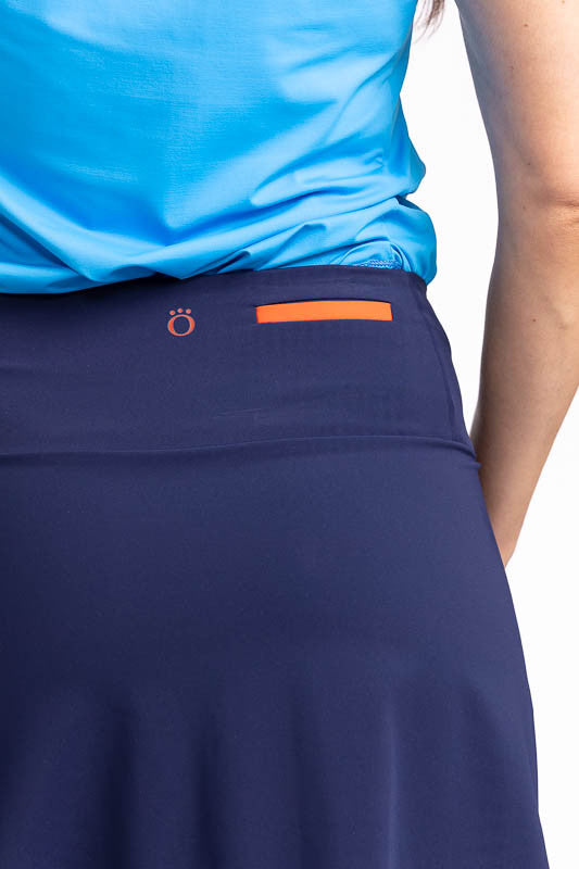 Close back view of the Long Strides Golf Skort in Navy Blue. This skort is a solid navy blue with two patch pockets that have a pacific blue stripe above the button and an orange stripe below the button on each pocket. The front also has three navy blue b