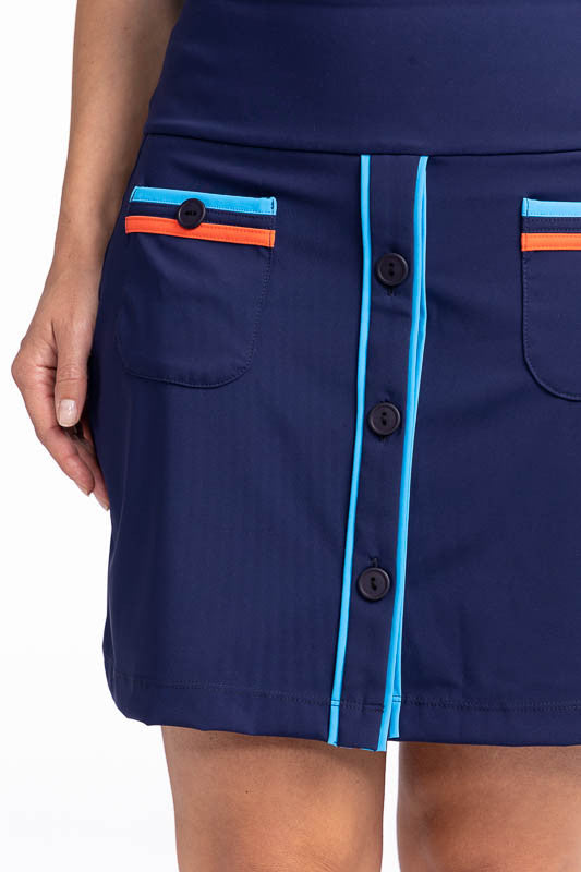 Close front and right side view of the Long Strides Golf Skort in Navy Blue. This skort is a solid navy blue with two patch pockets that have a pacific blue stripe above the button and an orange stripe below the button on each pocket. The front also has t
