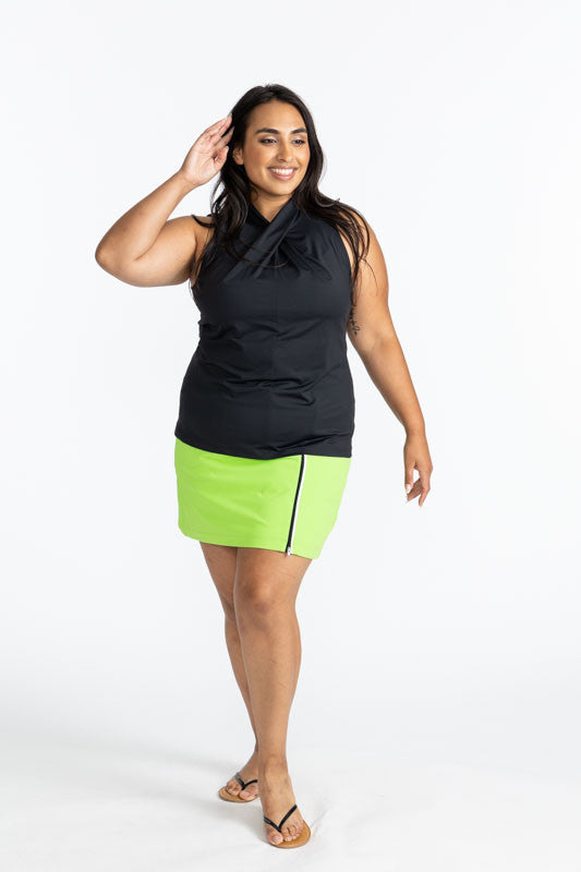 Full front view of a smiling woman wearing the Twist and Shout Sleeveless Golf Top in Black and the Summer Sass Golf Skort in Grass Green. This is a solid green skort with a 3/4 black zipper on the front left side. 
