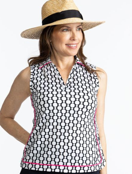 Smiling woman wearing a straw hat and the Bogey Round Sleeveless Golf Top in Spiral Floral. This is a retro-inspired abstract floral pattern in black and white.