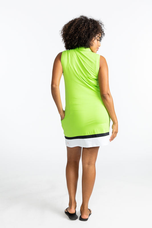 Full back view of a woman wearing the In Play Sleeveless Golf Dress in Grass Green. This dress is primarily grass green with a thin band of black near the bottom, followed by a thicker section of white at the bottom of this dress.