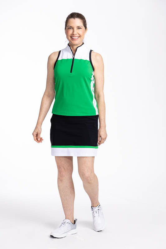 Full front view of a smiling woman wearing the In Play Golf Skort in Black/Green and the Resolution Sleeveless Golf Top in Rye Grass Green. This is a predominantly black skort with a thin band of green followed by a wide band of white at the bottom of the